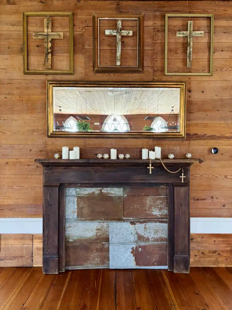 Reclaimed-wood mantel with candles and framed crosses inside O'Kelly Chapel